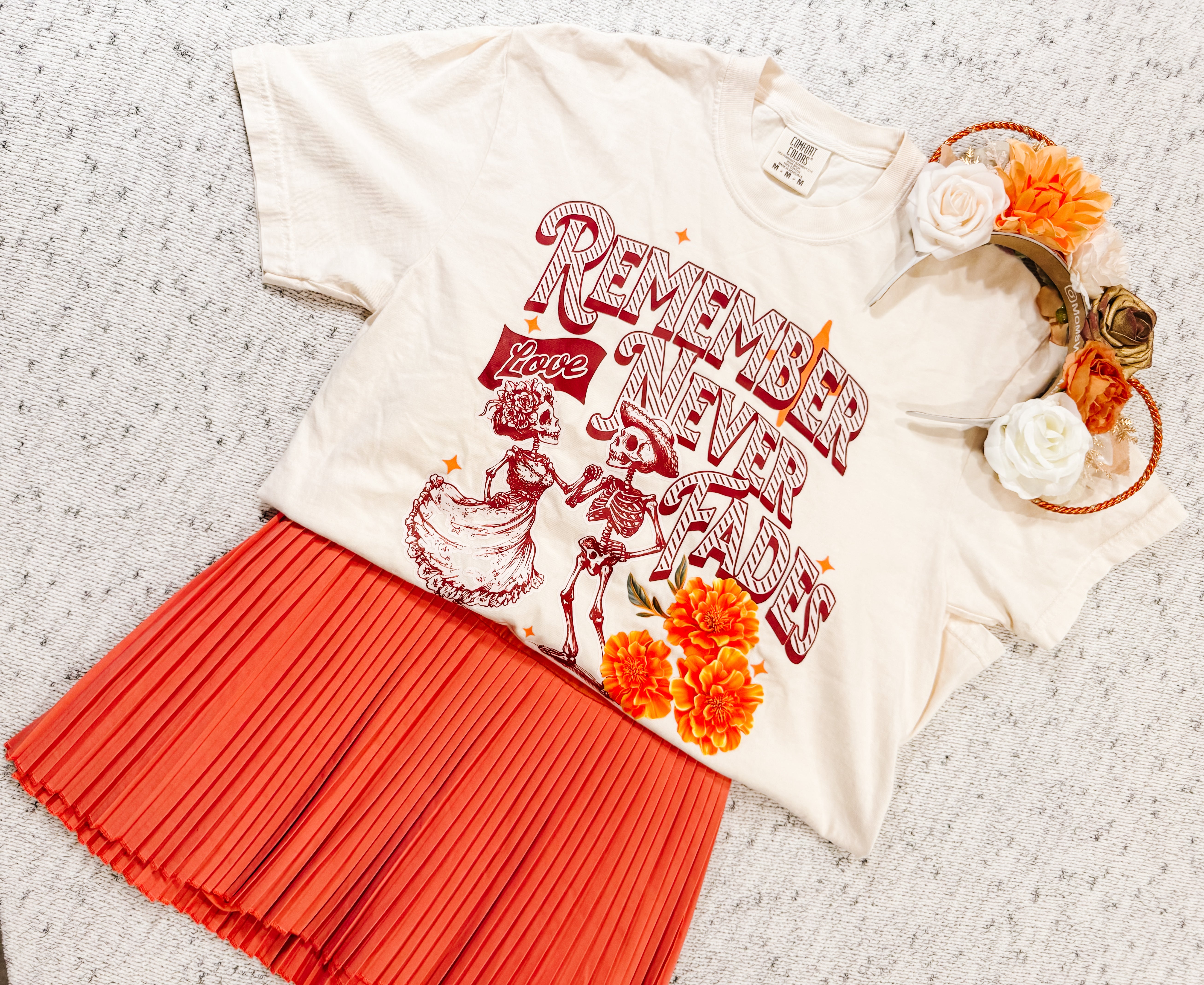 Day of the Dead inspired graphic tee with skeletons, orange pleated skirt, and floral headband